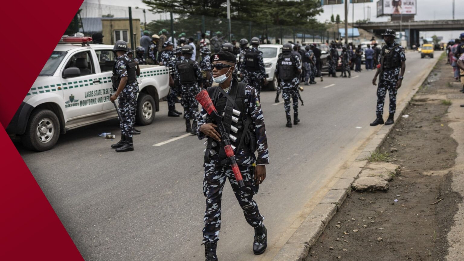 Armed Nigerian riot police in khaki uniforms and helmets confront a crowd of chanting protesters on a smoky Lagos street during political unrest